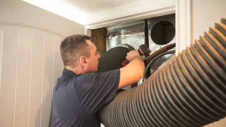 Technician installs or repairs large flexible ducting in HVAC system inside building interior.