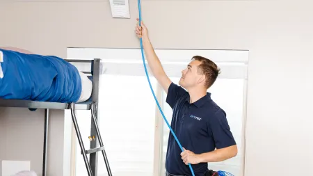 Technician installing blue Ethernet cable through ceiling vent in residential room with bunk bed.