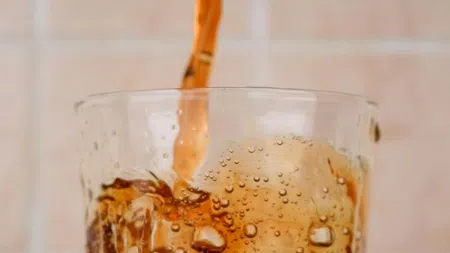 Carbonated soda being poured into a glass with ice cubes, creating bubbles and fizz in the drink.