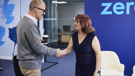 Man and woman shaking hands in modern office with blue wall and white chairs, professional greeting