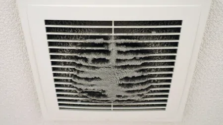Close-up of a ceiling air vent covered with thick, dusty buildup obstructing airflow