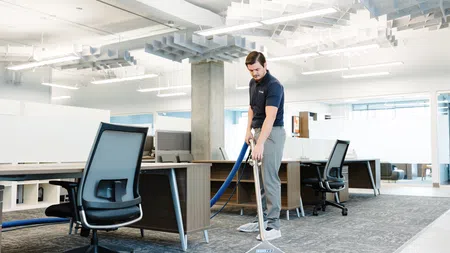Man cleaning office carpet using professional carpet cleaning equipment in a modern workspace.