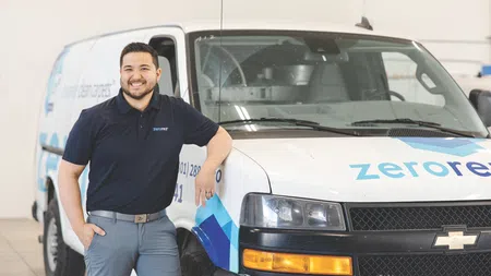 Smiling technician in branded polo stands beside a Chevrolet van with Zerorez logo in a service garage.