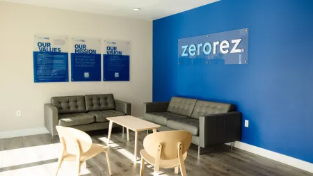 Modern office waiting area with gray sofas, wooden chairs, a table, blue accent wall with Zerorez logo, and company values displayed.