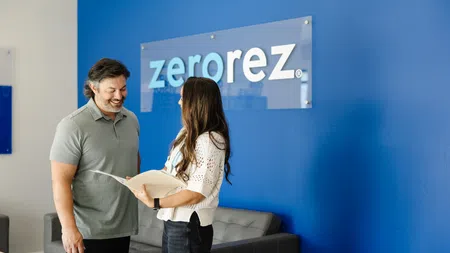 Man and woman reviewing documents in office with Zerorez logo on blue wall background