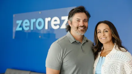 Smiling man and woman standing in front of a blue wall with a Zerorez logo sign