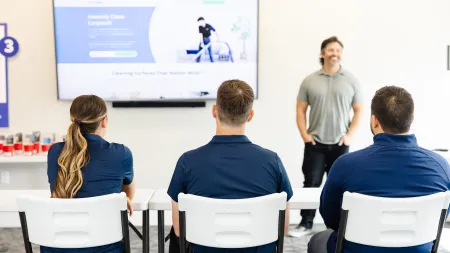 Three employees in navy shirts seated facing a presenter and a large screen during a training session.