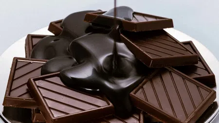 Rich melted chocolate cascading over a stack of dark chocolate bars on a reflective plate.