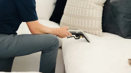 a male white Zerorez technician kneeling and using an upholstery tool to clean stains on microfiber couch that's white