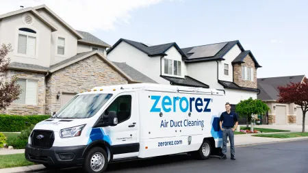 A Zerorez air duct cleaning van parked in front of a modern home with a technician ready for service.