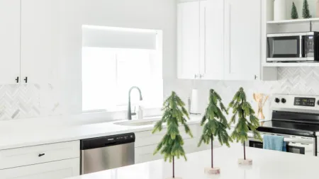 Bright modern white kitchen with three small decorative pine trees on the island countertop under natural light.