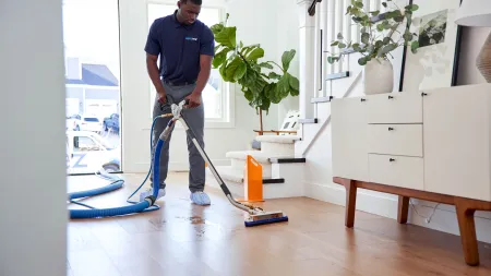 Professional cleaner using a floor cleaning machine on hardwood floor in a bright modern home interior.