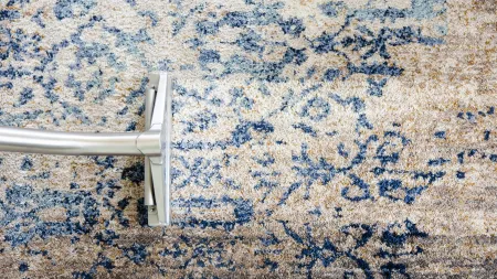 Vacuum cleaner cleaning a patterned blue and beige carpet with visible clean and dirty areas.