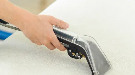 A person using a steam cleaner on a light-colored couch to remove dirt and stains effectively.