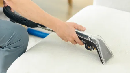 a Zerorez technician holding an upholstery tool on a white couch to help clean it as part of the carpet beetle removal process in a home for furniture and upholstery