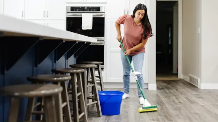 a woman mopping a hardwood floor in her kitchen with soapy water in a blue bucket