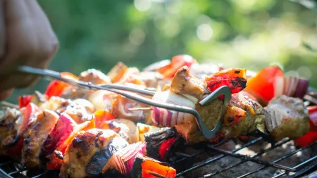 Close-up of grilled meat and vegetable skewers being turned on a round charcoal barbecue grill outdoors.