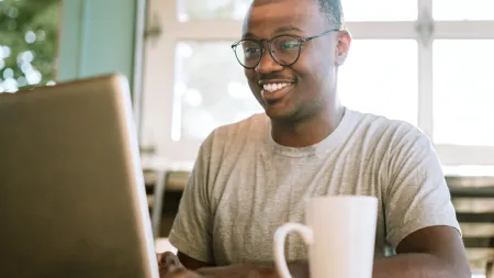 a man sitting at a table with a laptop and a mug