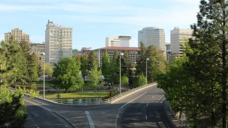 Cityscape with tall buildings, green trees, a park, and a curved road under clear blue sky.
