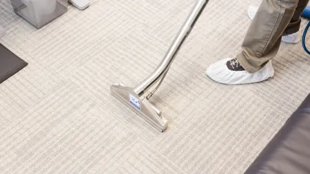 Professional cleaning of light-colored office carpet using a carpet cleaning machine and shoe covers.