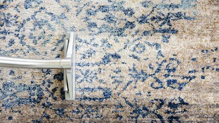 Vacuum cleaner cleaning a beige and blue patterned carpet revealing a cleaner section.