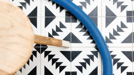 Close-up of black and white geometric tiled floor with a blue flexible hose and a wooden chair leg.
