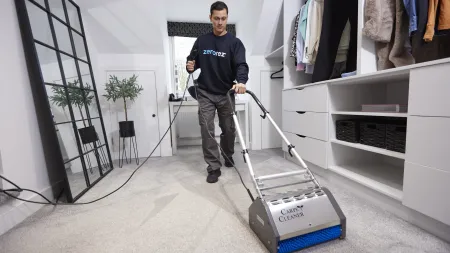 Man using a carpet cleaner machine to clean carpet in a modern walk-in closet with clothes and mirror.