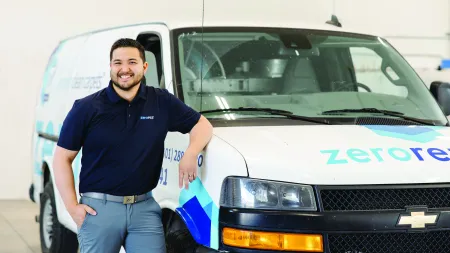 Smiling man in navy polo stands next to a white Chevrolet van branded with Zerorez logo inside a bright garage.
