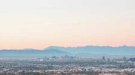 Wide aerial view of a sprawling cityscape with distant mountain range under a soft pastel sky at sunrise.