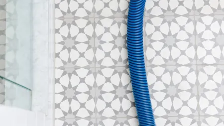 a blue Zerorez cleaning hose on a white and gray patterned tile bathroom floor