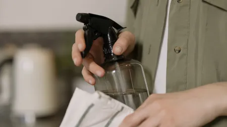 Person holding a spray bottle and a cloth in a kitchen setting, ready to clean.