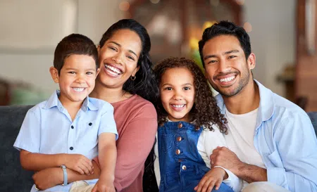 Smiling happy family of four sitting closely together on a couch indoors, showing warmth and love