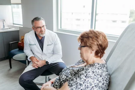 Doctor in white coat consulting with a seated female patient in a modern medical office with natural light.