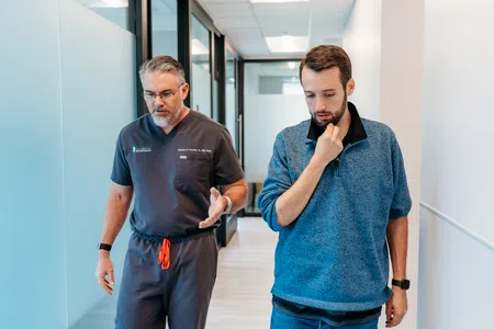 Doctor in scrubs discussing with a patient walking down a medical office hallway