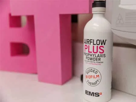 Bottle of AIRFLOW PLUS Prophylaxis Powder for dental biofilm therapy with pink letters and EMS logo.