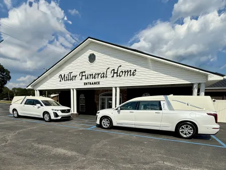 Two white hearses parked in front of Miller Funeral Home under a blue sky with scattered clouds.