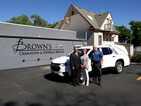 Three people stand by a white vehicle outside Brown's Cremation and Funeral Service building.