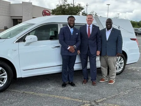 Three men in suits standing beside a white Platinum hearse