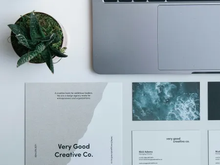 Workspace featuring a laptop, two succulents, and Very Good Creative Co. branded business cards and brochure.