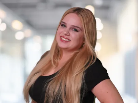 Smiling woman with long blonde hair wearing a black shirt posing with hand on hip indoors