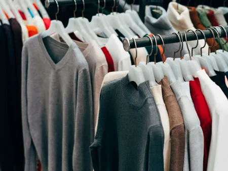 Rows of sweaters in various colors hanging on racks at a clothing store or market display.