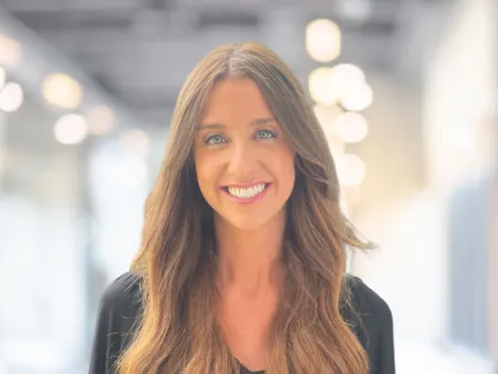 Smiling woman with long wavy brown hair wearing a black top in a bright modern office setting