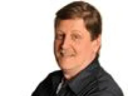 Man standing with arms crossed wearing a black shirt, white long sleeves, blue jeans, and brown shoes