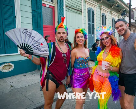Four colorful, lively people in festive rainbow outfits posing on a New Orleans street during a celebration.
