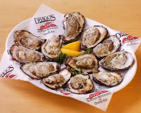Grilled oysters on a white plate with lemon wedges, served on branded paper from Drago's Seafood Restaurant.