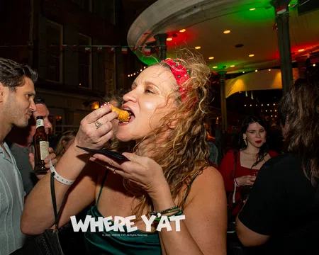 Woman in red headband eating fried food at lively nighttime party with people drinking and socializing.