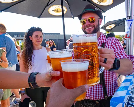 Group of people clinking large beer mugs and cups at an outdoor festival under branded umbrellas