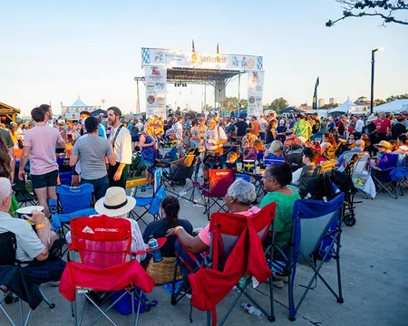 Crowd enjoying an outdoor music festival with people sitting on chairs and socializing near the stage at sunset.