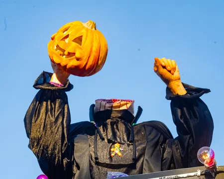 Headless Halloween figure in black costume holding a carved pumpkin against a clear blue sky.