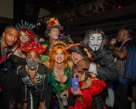 Group of adults in colorful and creative costumes posing indoors at a lively Halloween or costume party.